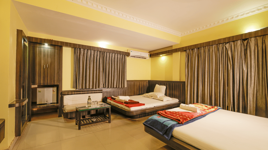 A bedroom with 2 king beds, a sofa, a coffee table, a mini fridge, curtains, and a wardrobe at Hotel Seagull Digha.